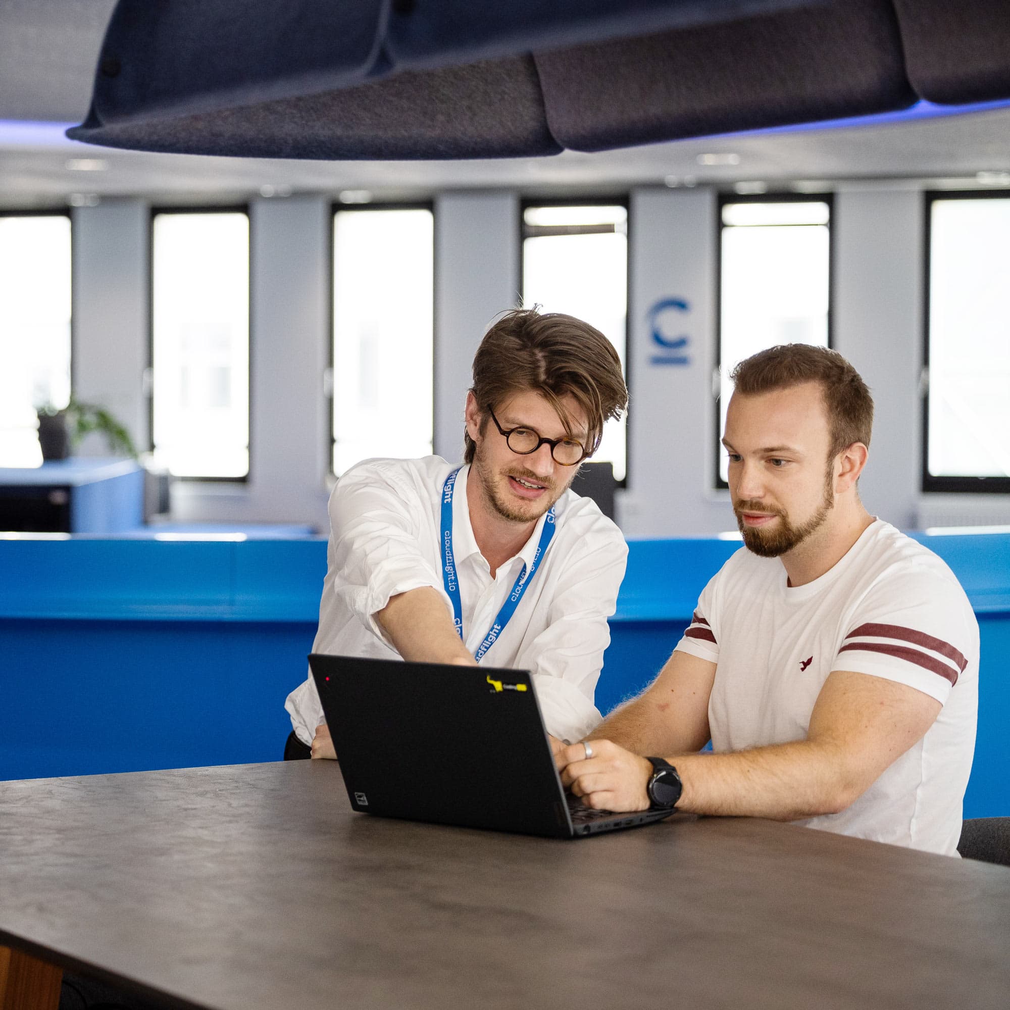 The image shows two engineers working on a laptop.